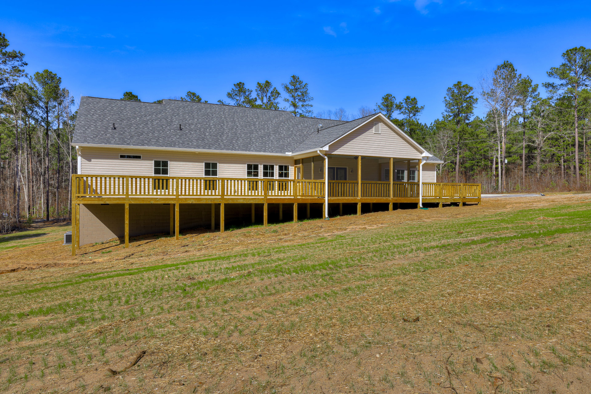 White siding house with covered porch, wooden deck, and manicured lawn; mature trees and power lines in background under partly cloudy sky