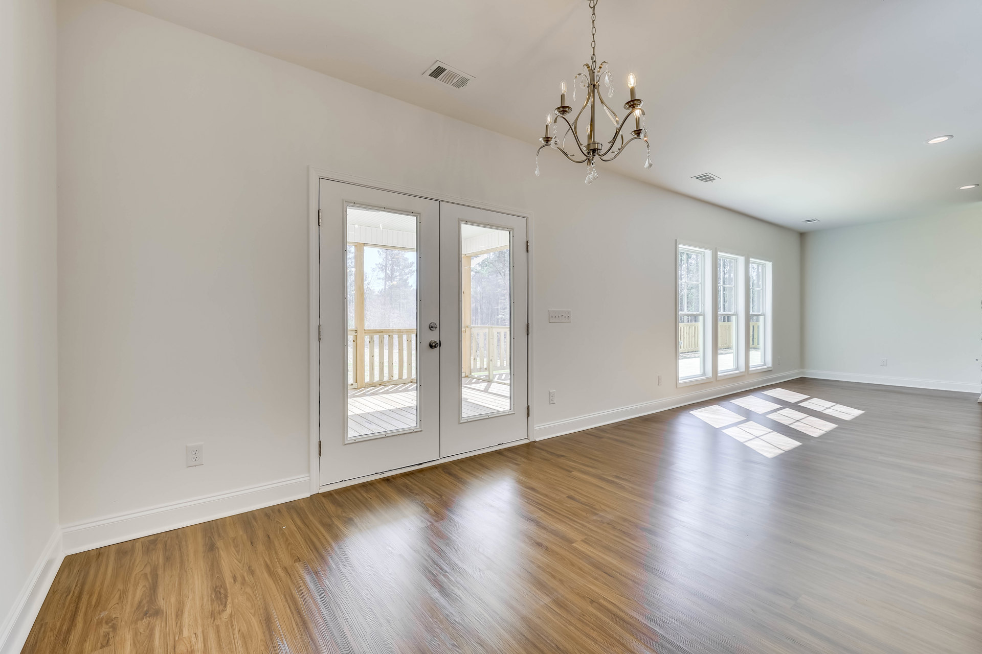 Chandelier with multiple lights hanging from ceiling above wood floor, double glass doors framed in white, white walls, and square tile inlay on floor