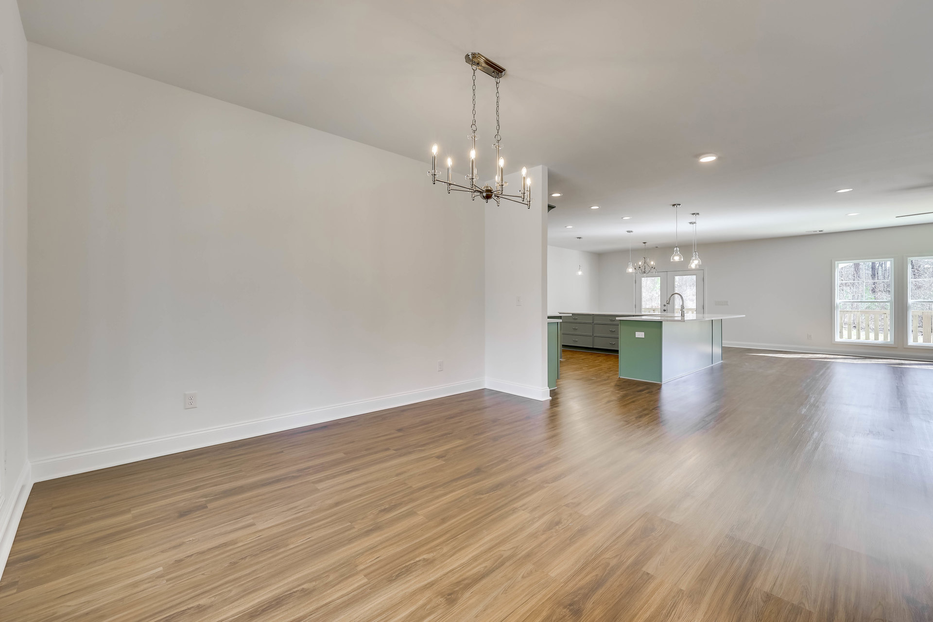 Open kitchen with hardwood flooring, green accent wall, modern chandelier, large window overlooking trees, and close-up of wood cabinetry drawer.