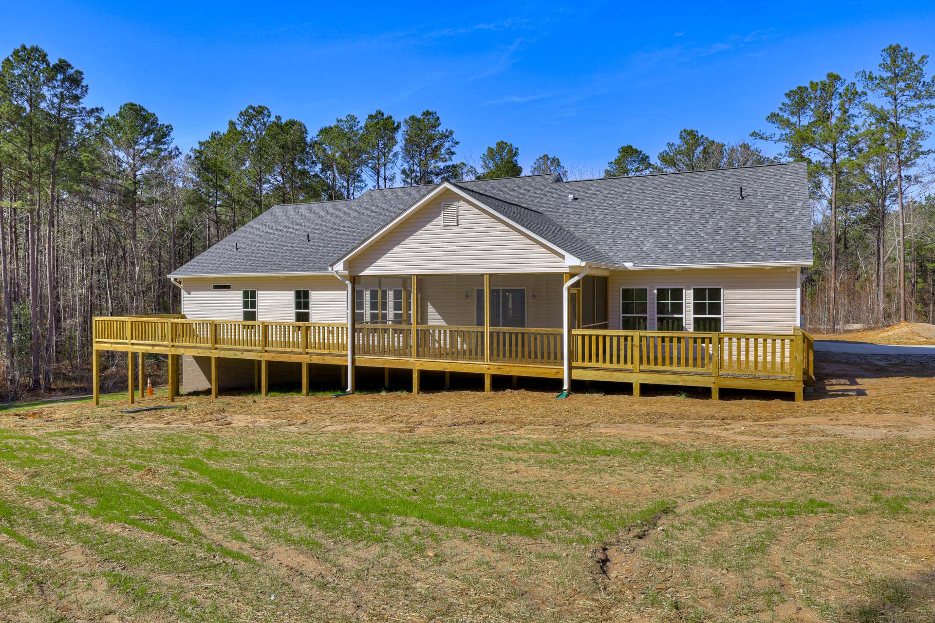 Two-story home with screened porch, wooden deck, white-framed windows, and expansive grassy yard bordered by trees.