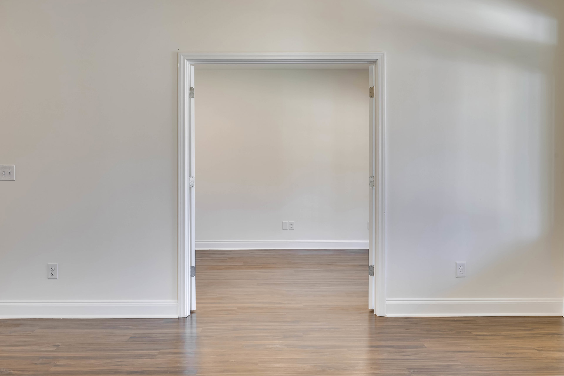 White walls, light brown wood floor, open white door with white frame, refrigerator partially visible in doorway