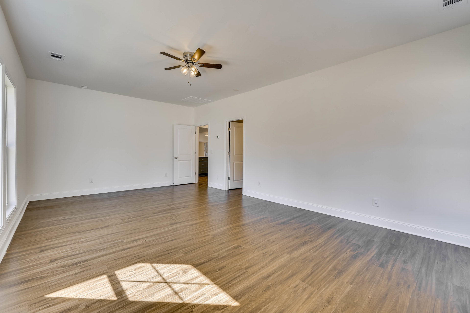 Ceiling fan with lights mounted above wood flooring, white plaster walls, and a white door in a residential interior.
