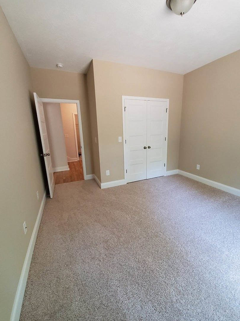 Beige carpeted room with white double doors, silver handles, and white walls