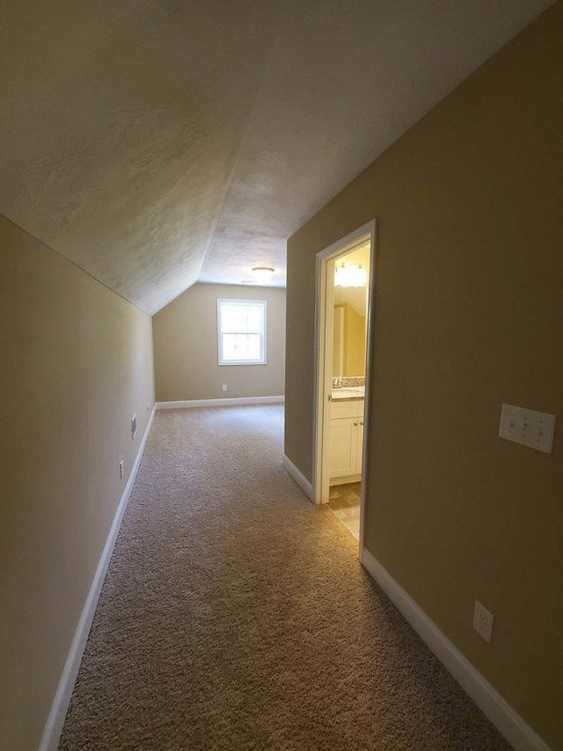 Hallway with light-colored walls, white door partially open, white-framed window, white wall outlet, and wood flooring