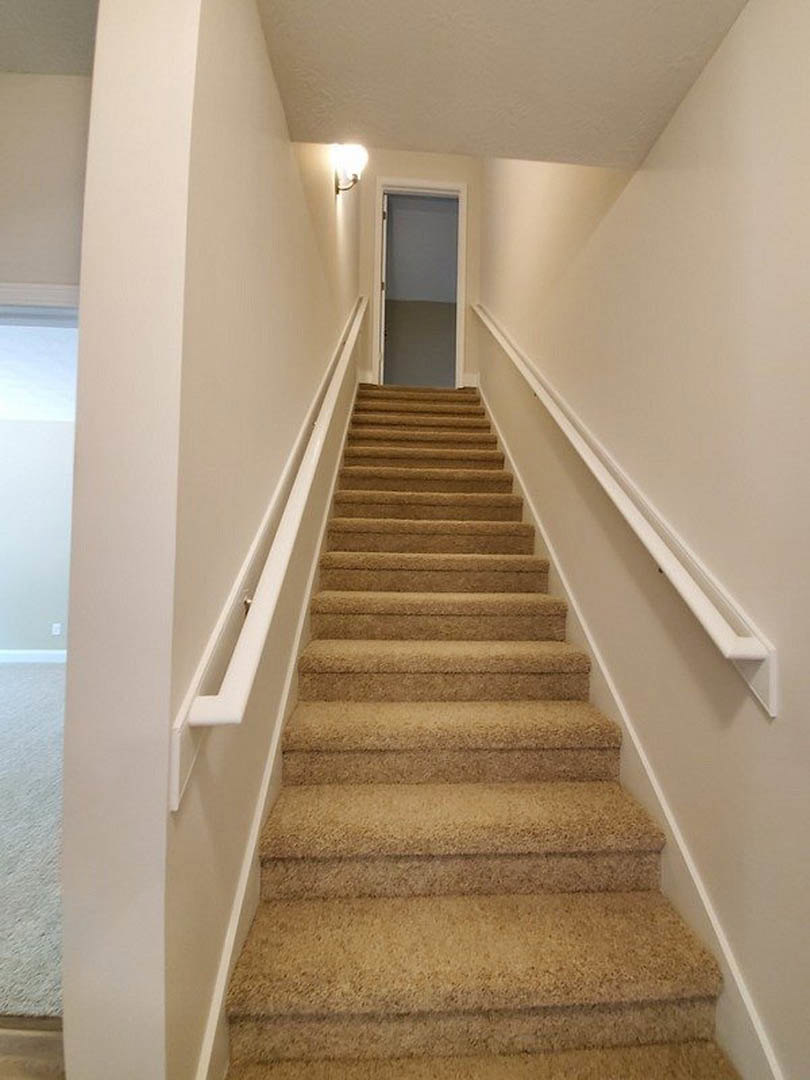 Beige carpeted staircase with wooden handrail, open white door at landing, plaster walls, and partial view of mirror in adjacent room