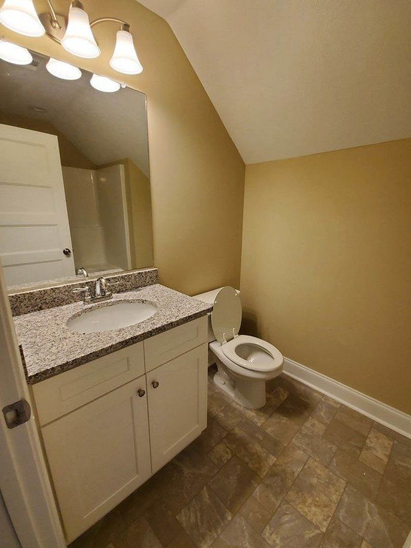 White porcelain sink with chrome faucet set in a stone countertop, toilet with lid up, light fixture above, and patterned tile flooring in a modern bathroom.