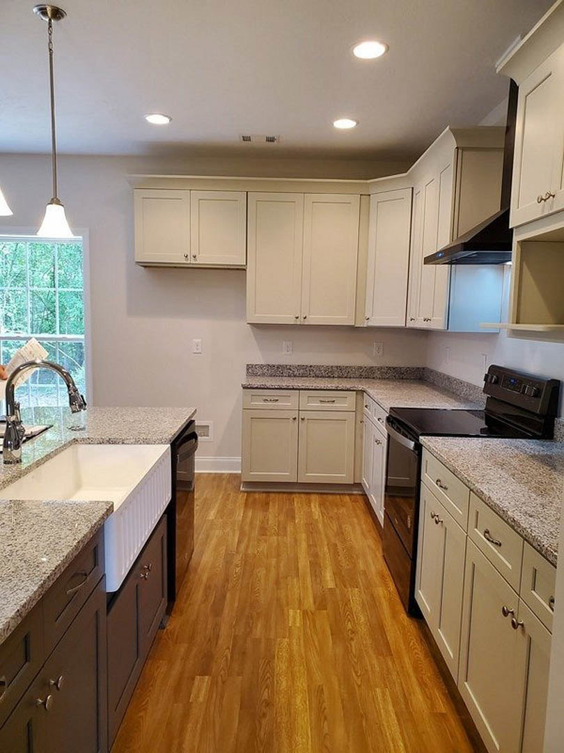 Granite kitchen countertops with wood flooring, paneled cabinetry, stainless faucet, multi-pane window, and pendant light fixture