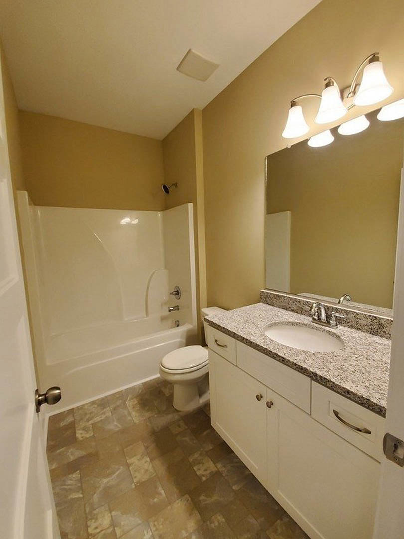 Modern bathroom with white tile walls, glass-enclosed shower, rectangular sink with chrome faucet, wall-mounted lighting, and white toilet adjacent to a freestanding bathtub