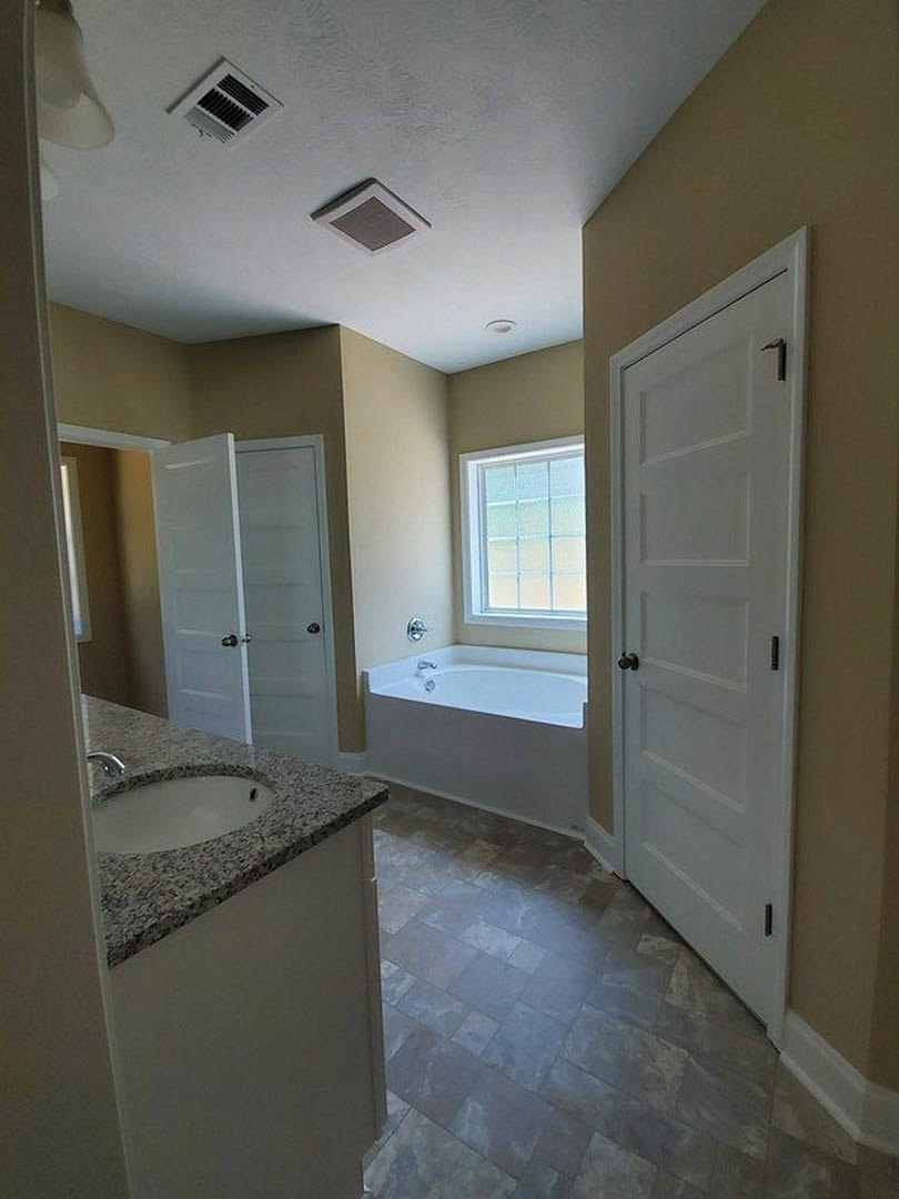 Bathroom with white tile floor, freestanding bathtub, white sink vanity, window with natural light, and white paneled door with silver doorknob