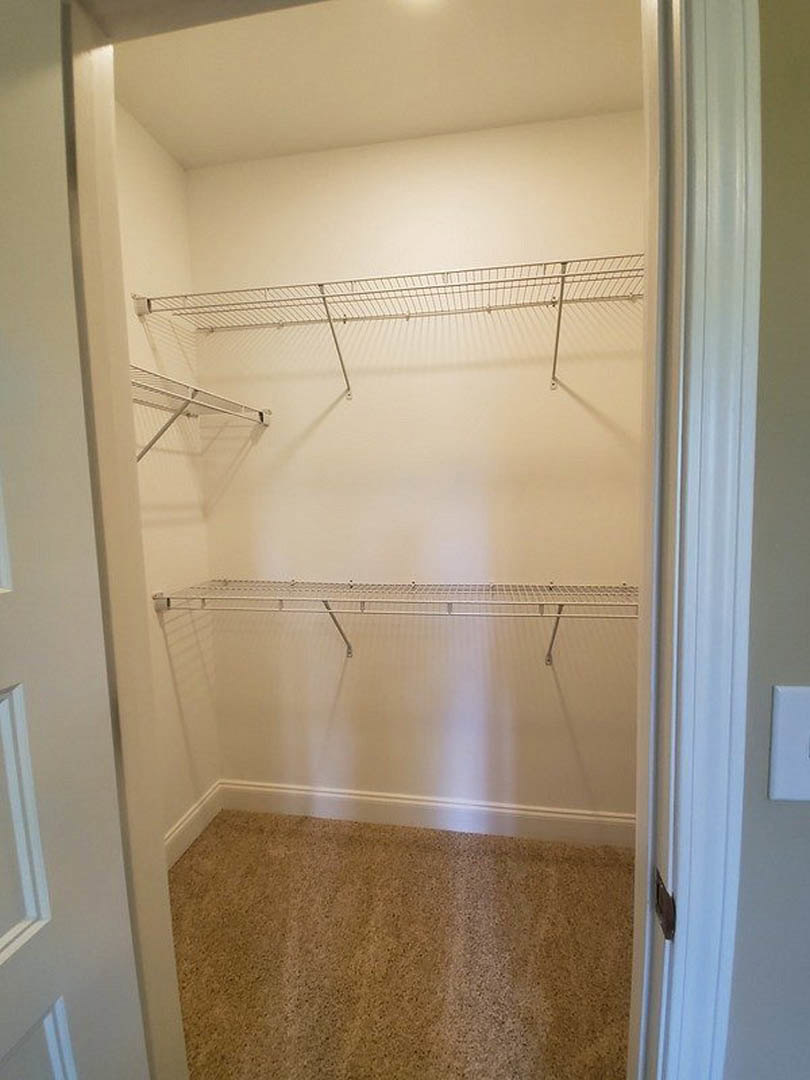Walk-in closet with white shelving, metal hanging rods, and light-colored carpet flooring