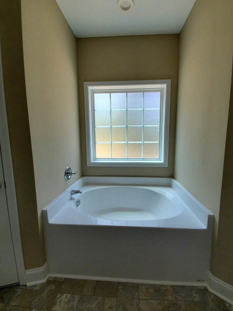 White freestanding bathtub with silver faucets beside frosted glass window, white tile floor, and chrome handle in modern bathroom.