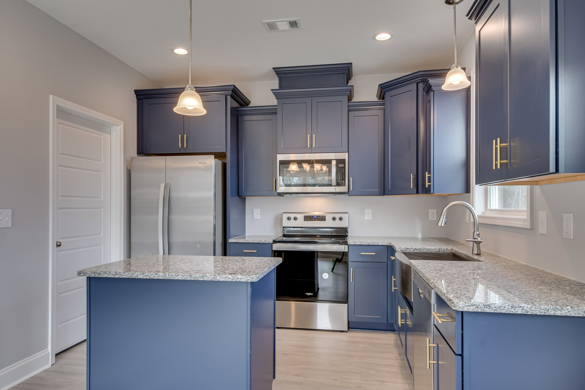 Blue kitchen cabinets with brushed hardware, granite countertops, stainless steel oven and refrigerator, ceiling light fixture reflected in window, under-mount sink, and drawers.