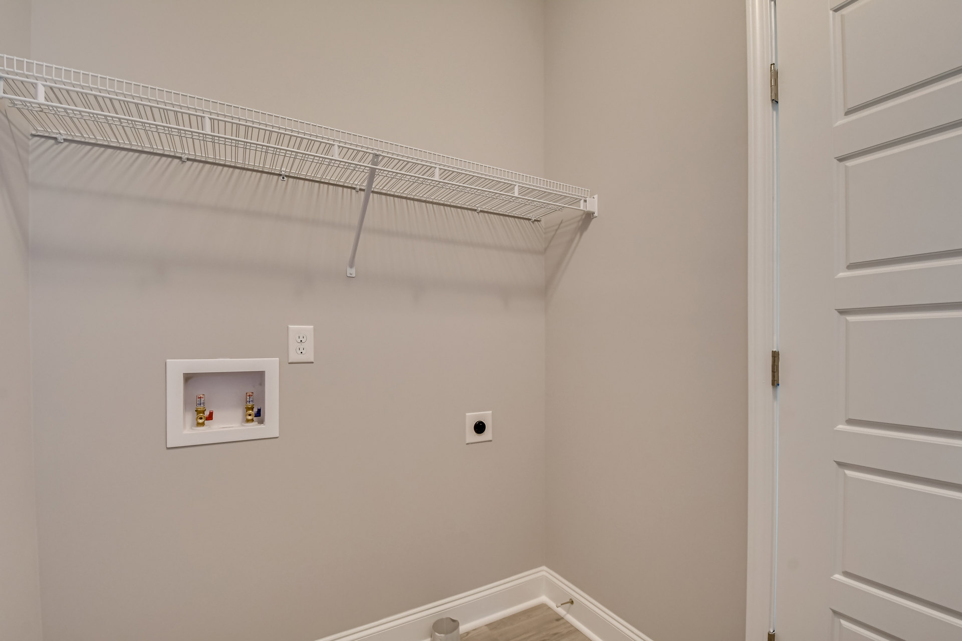 White wire rack mounted on a plaster bathroom wall near a white door with hinge, electrical outlet, and shower valve box.