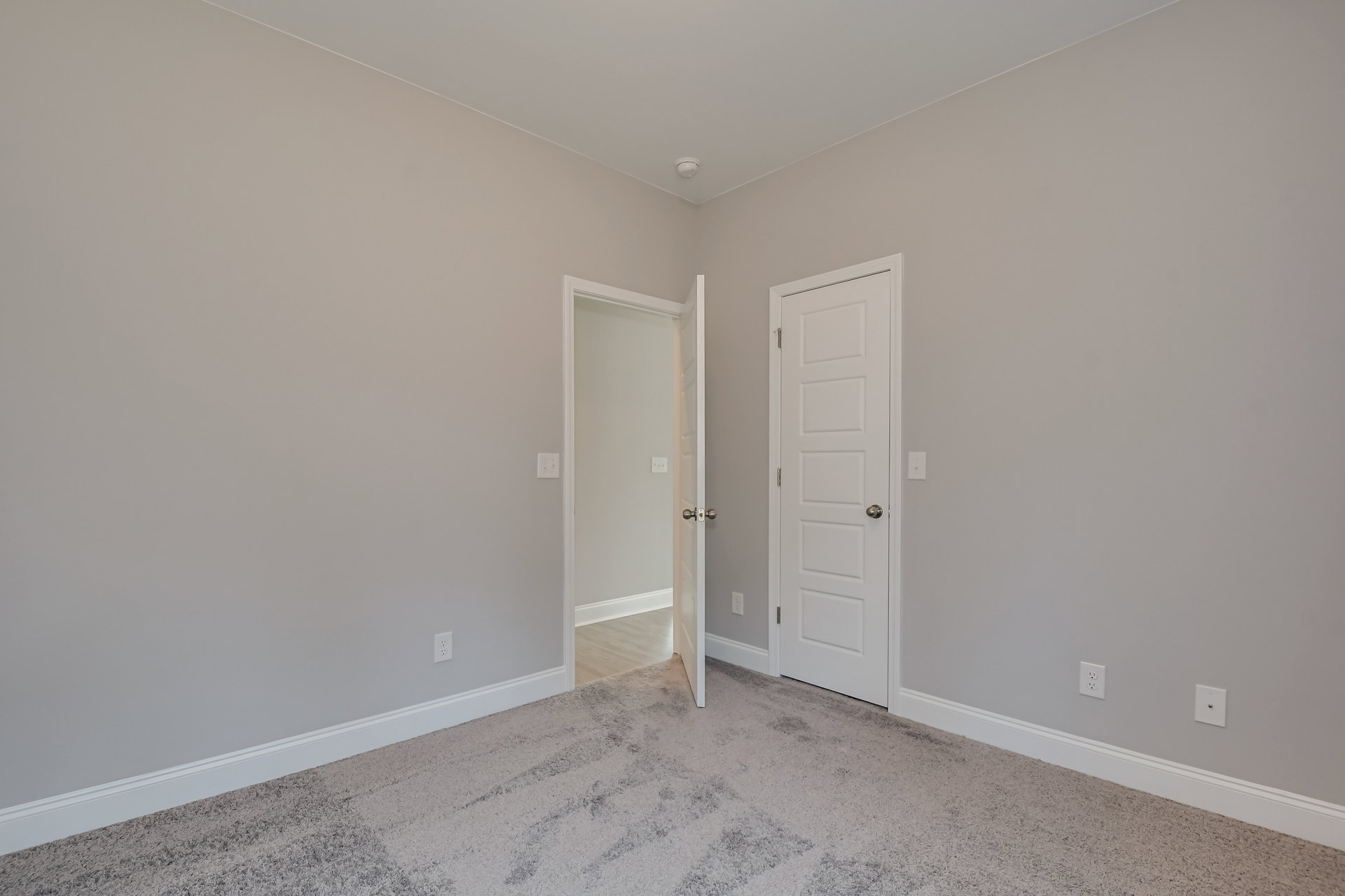 Carpeted room with two open white doors, silver door knobs, white plaster walls, and ceiling.
