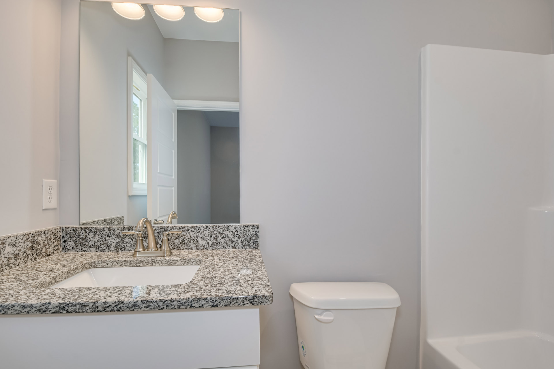 Marble countertop with undermount sink and chrome faucet, white toilet, white tiled wall, electrical outlet, bathtub partially visible