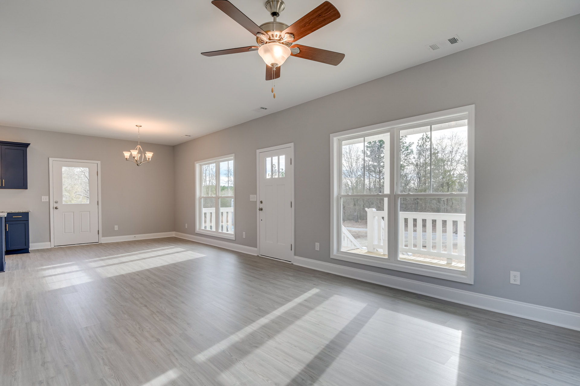 Ceiling fan with light fixture, wood laminate flooring, white plaster walls, large windows, white door with glass panel, chandelier hanging from ceiling