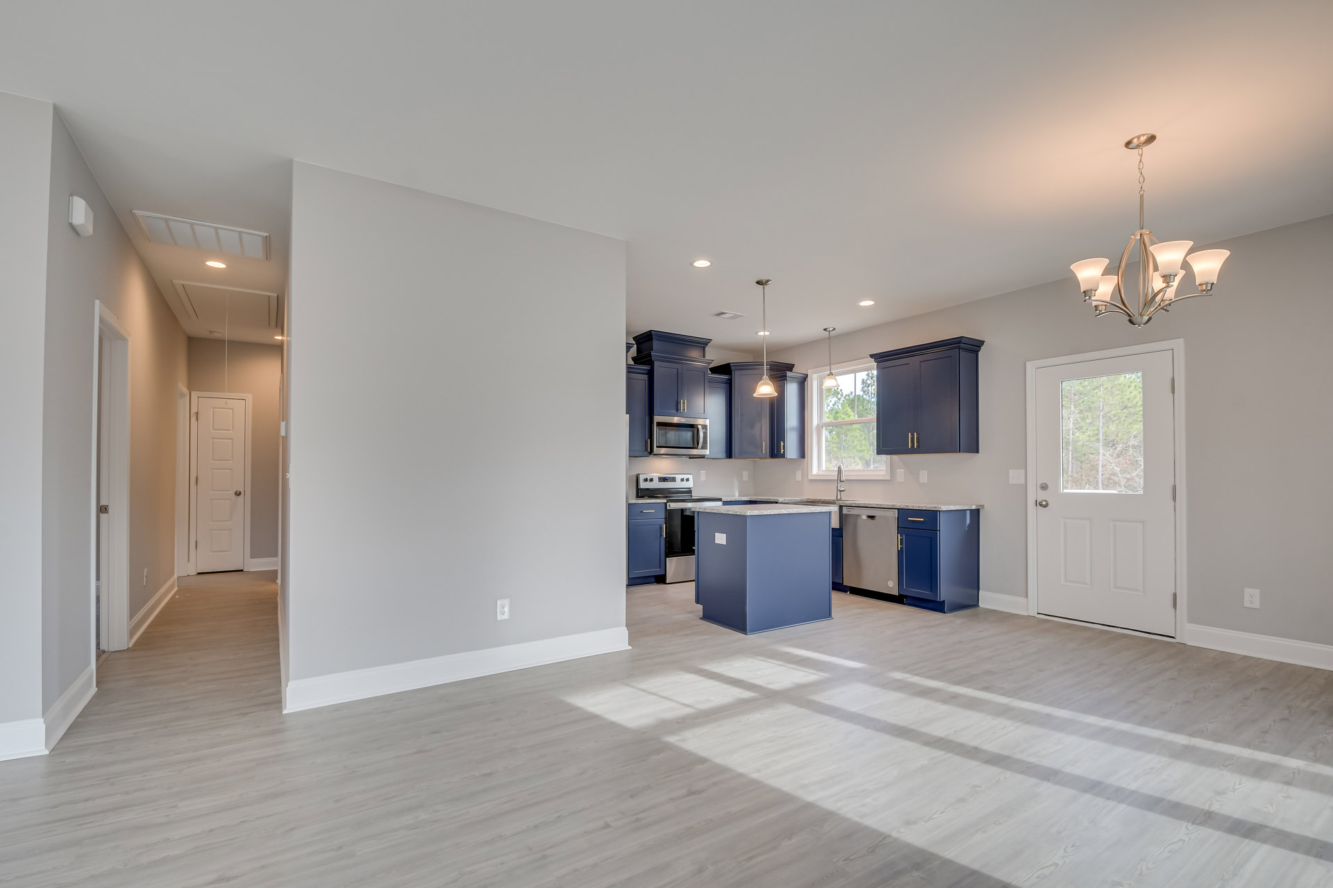 Open kitchen and dining area featuring a central island with white countertop, white cabinetry, light wood flooring, white walls, a white door with window, and a modern chandelier