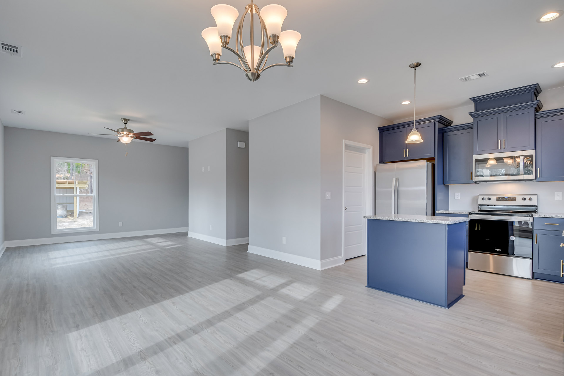 Open-concept kitchen and living room featuring a five-light chandelier, blue marble-topped counter, open stove door, wood shelf with bucket beneath window, cabinetry, and microwave