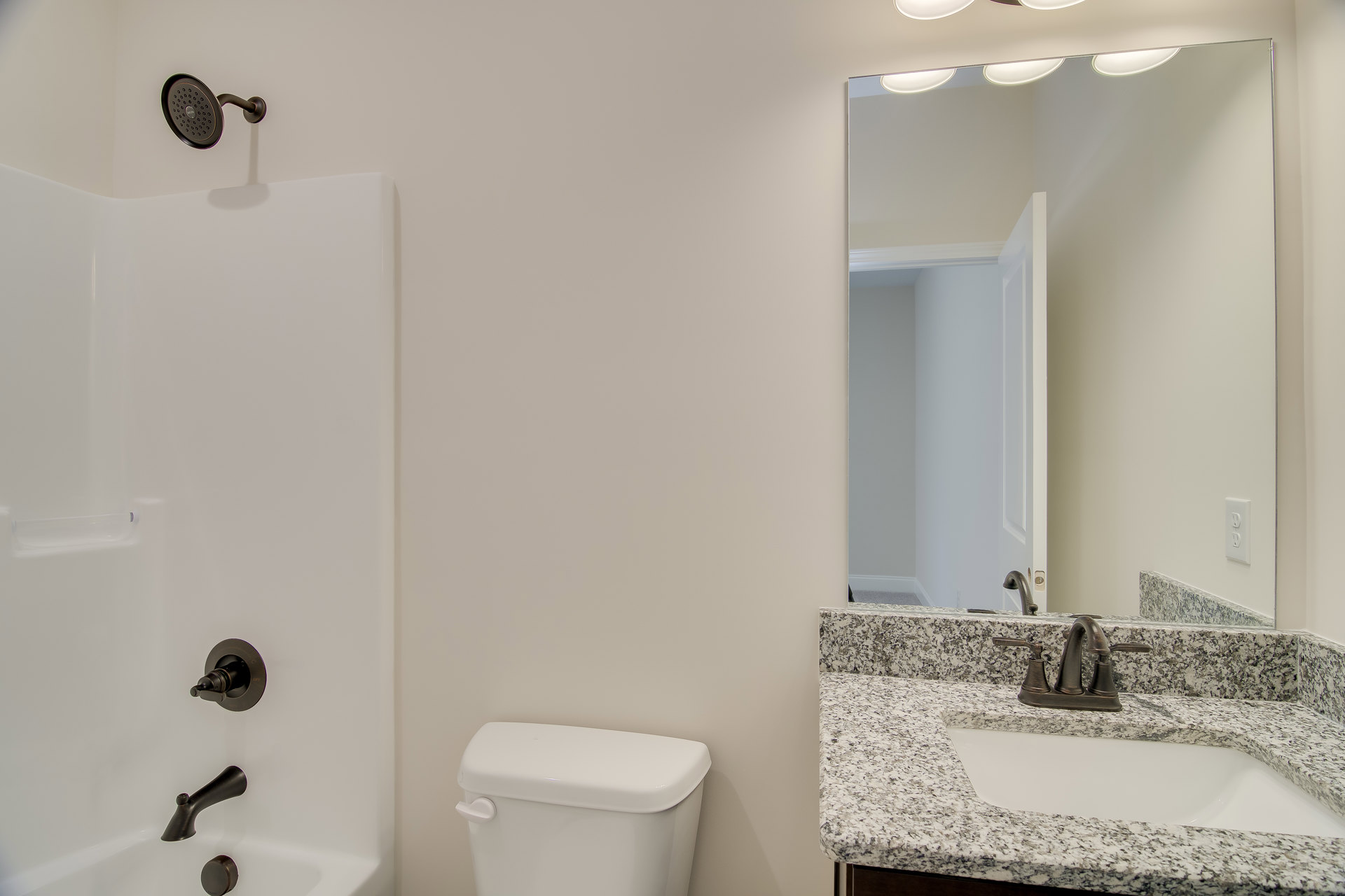 Modern bathroom with white porcelain sink and chrome faucet, adjacent toilet with closed lid, tiled walls, bathtub partially visible, and metal showerhead.