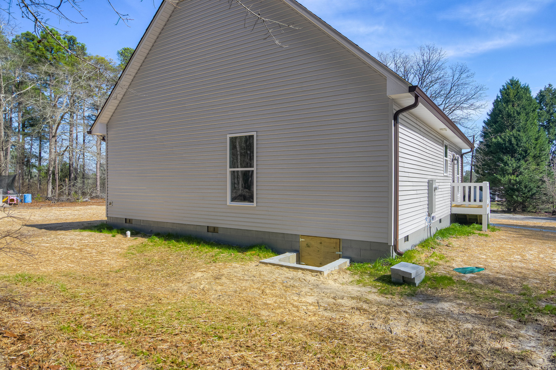 White cottage-style home with large windows, small front door, grey brick accents, white wooden deck, expansive green lawn, and mature leafy tree in the yard.