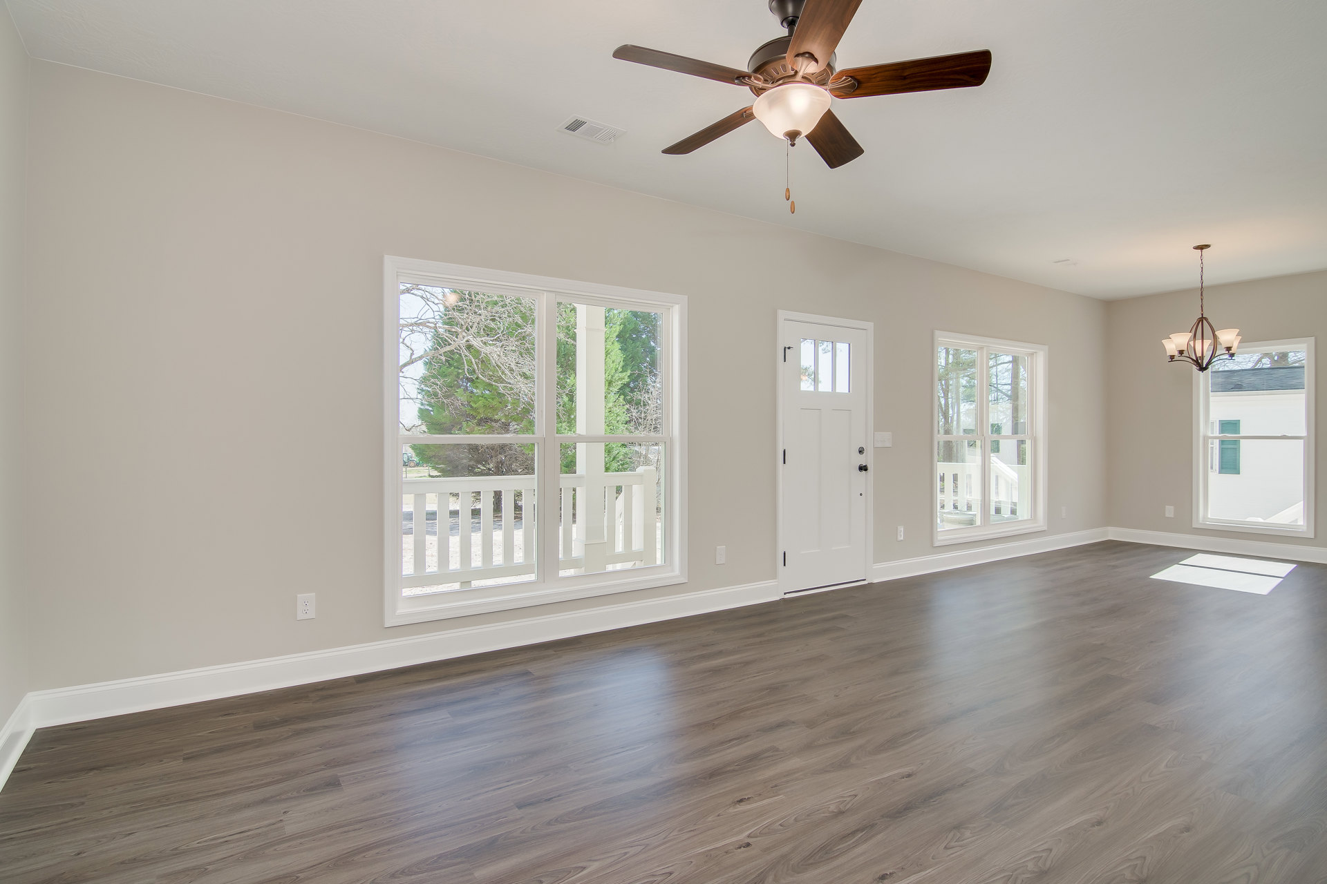 Hardwood floor room with white walls, ceiling fan with light fixture, multiple windows framed in white showing porch and trees outside, white door with glass window, crown molding
