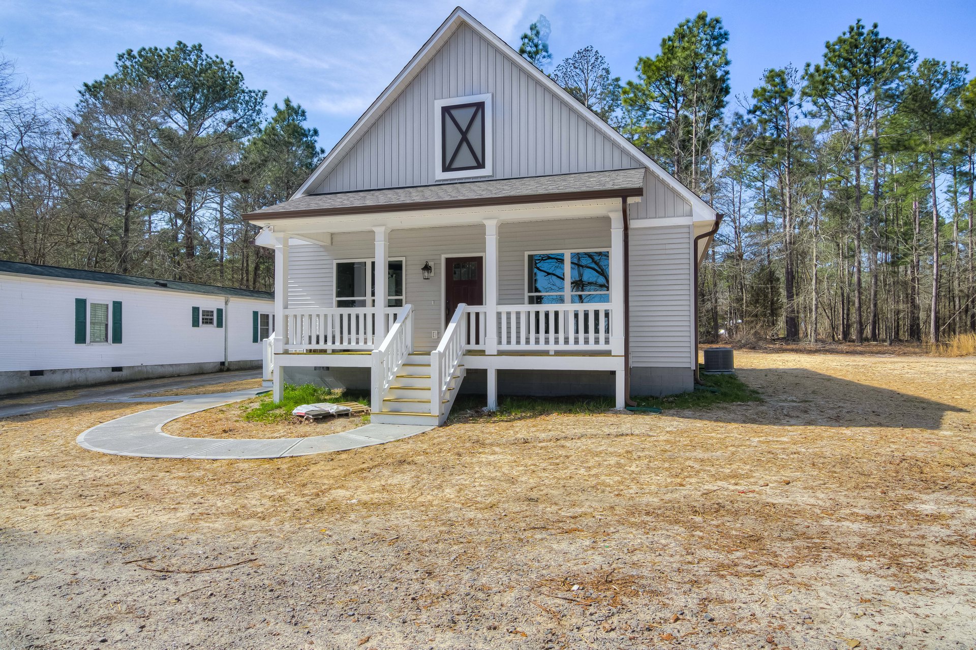 Two-story home with covered front porch, white railing, concrete driveway, large windows, and landscaped yard with trees and shrubs