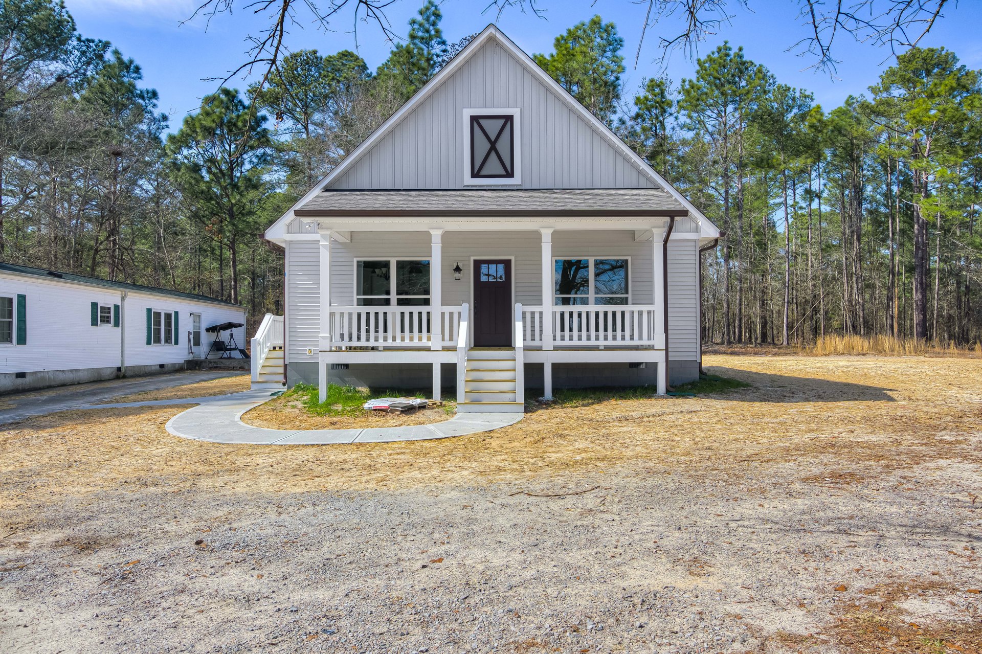White house with green shutters, black front door, and white porch, surrounded by trees and a paved driveway