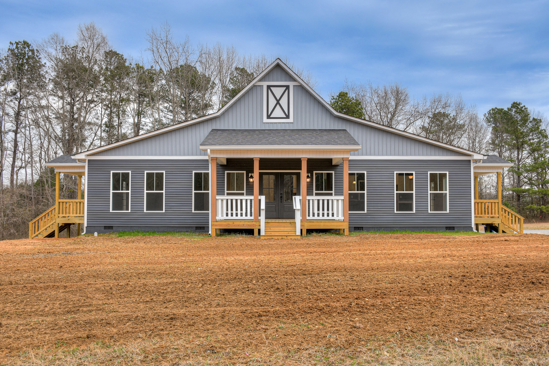White siding house with black trim, covered front porch, wide grassy yard, multiple windows, mature trees, cloudy sky