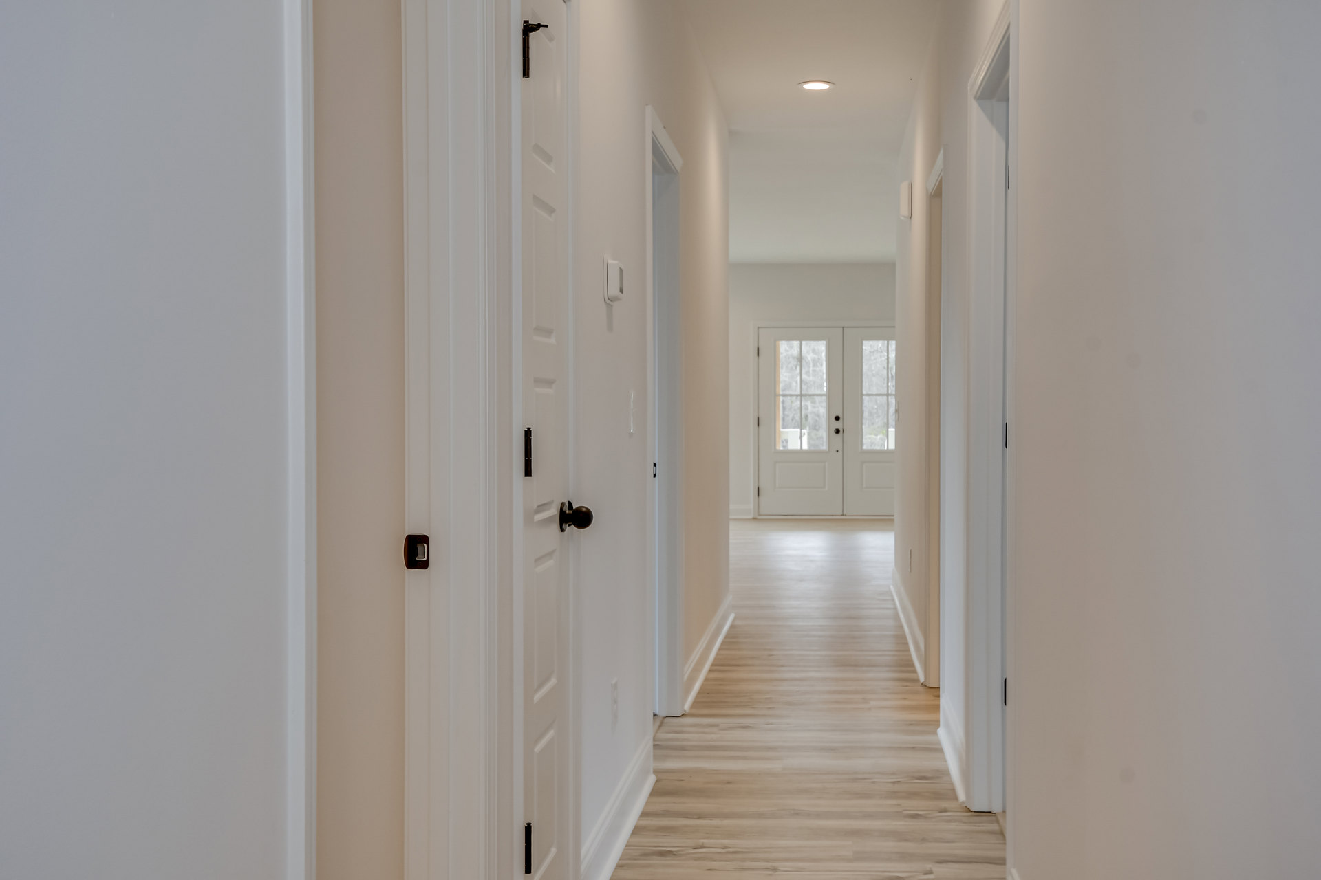 Hallway with wood flooring, white walls, white trim, and double white doors with glass panes