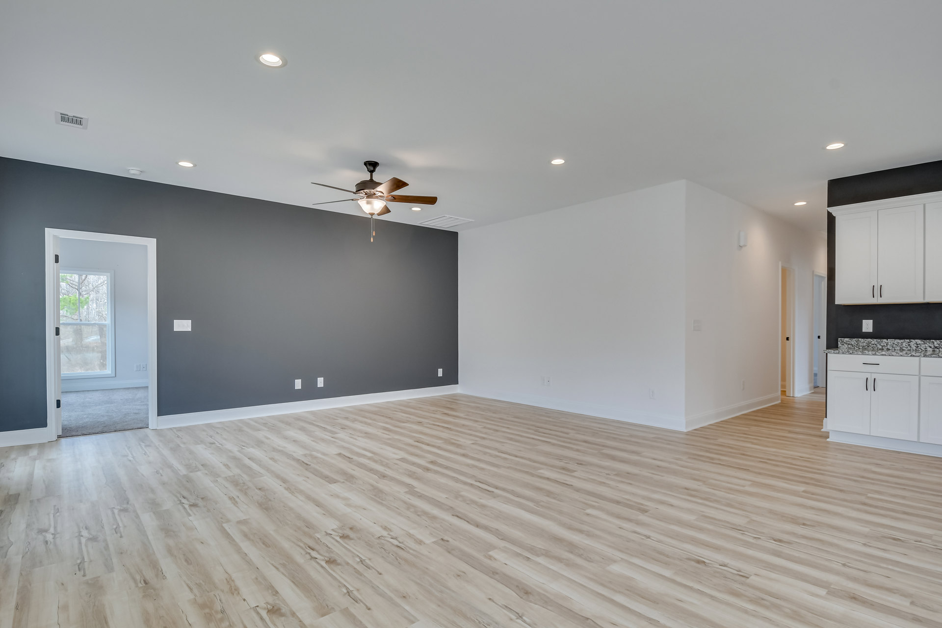 Ceiling fan with light fixture, wood flooring, white cabinets with black trim, door, window revealing tree outside