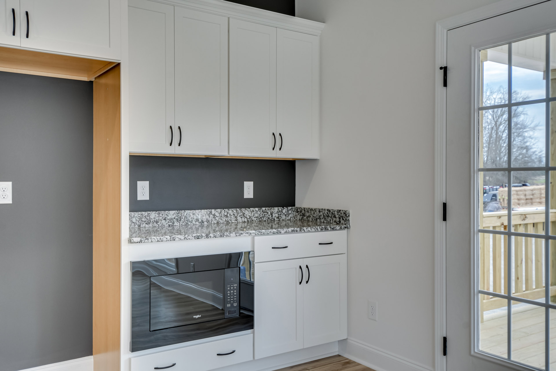 White kitchen cabinets with black handles, black microwave oven with glass door, light countertops, stainless steel sink, window overlooking fence and parked truck.