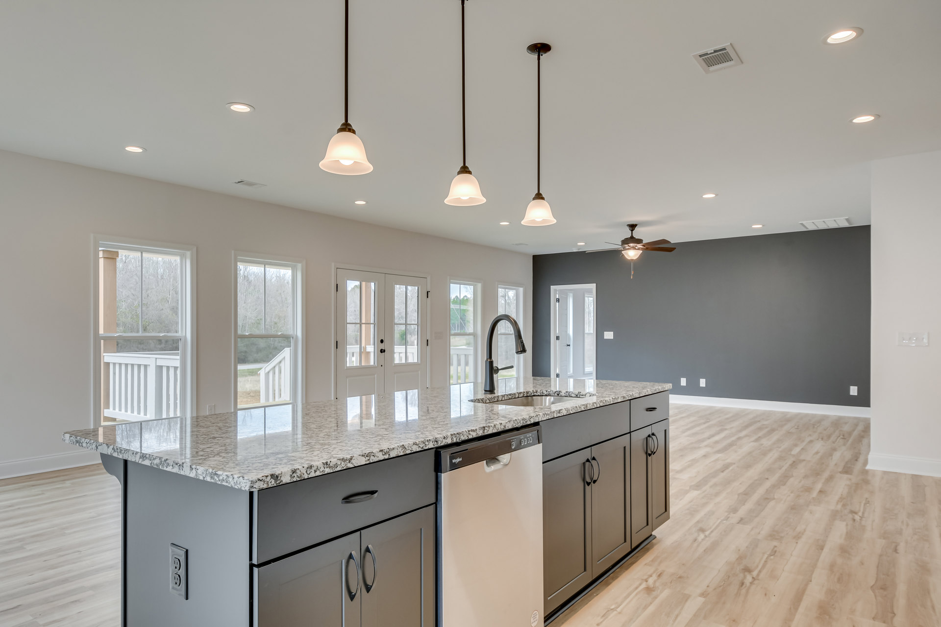 Spacious kitchen featuring a large central island with white granite countertops, built-in sink, stainless steel appliances, dark cabinetry, and ceiling vent