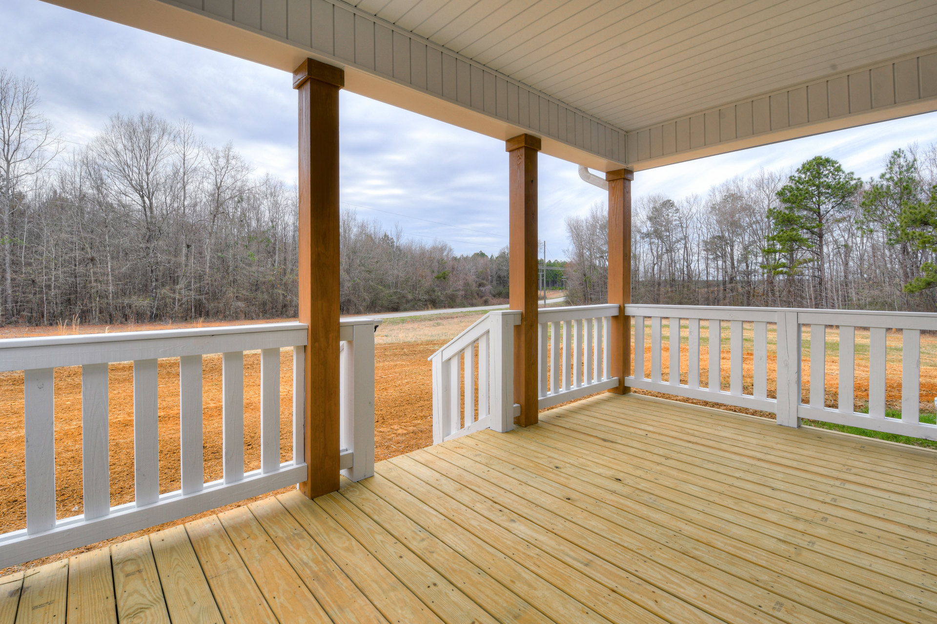 Spacious deck with white railing and wood pillars overlooking open field and dense trees, under a white roof