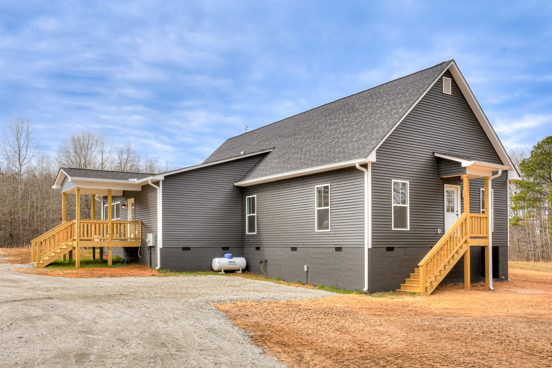 Two-story home with light siding, covered front porch, wooden steps, white-framed windows, driveway, and landscaped yard with trees.