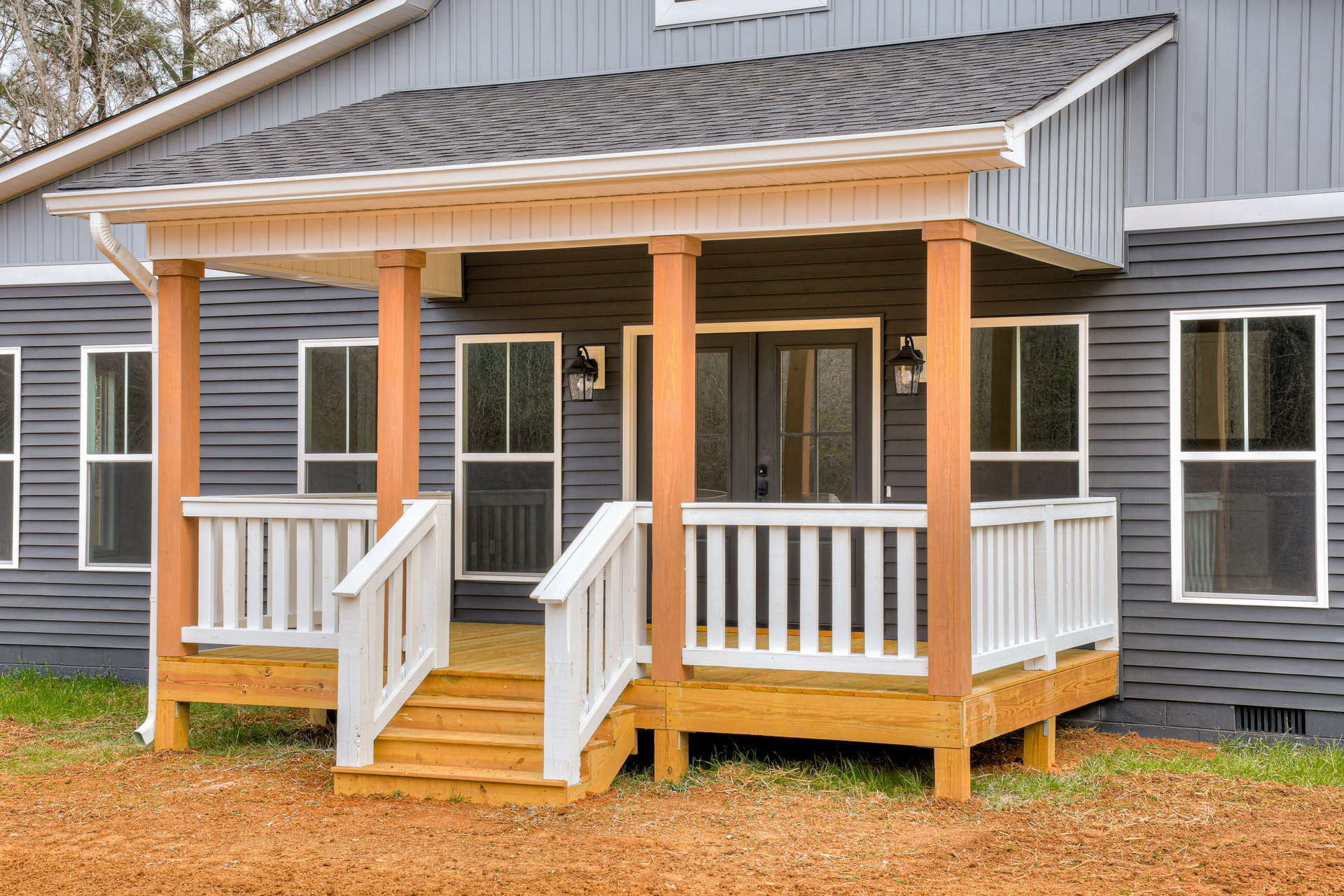 Two-story wooden home with covered front porch, white siding, stairs leading to entrance, multiple windows, and gabled roof
