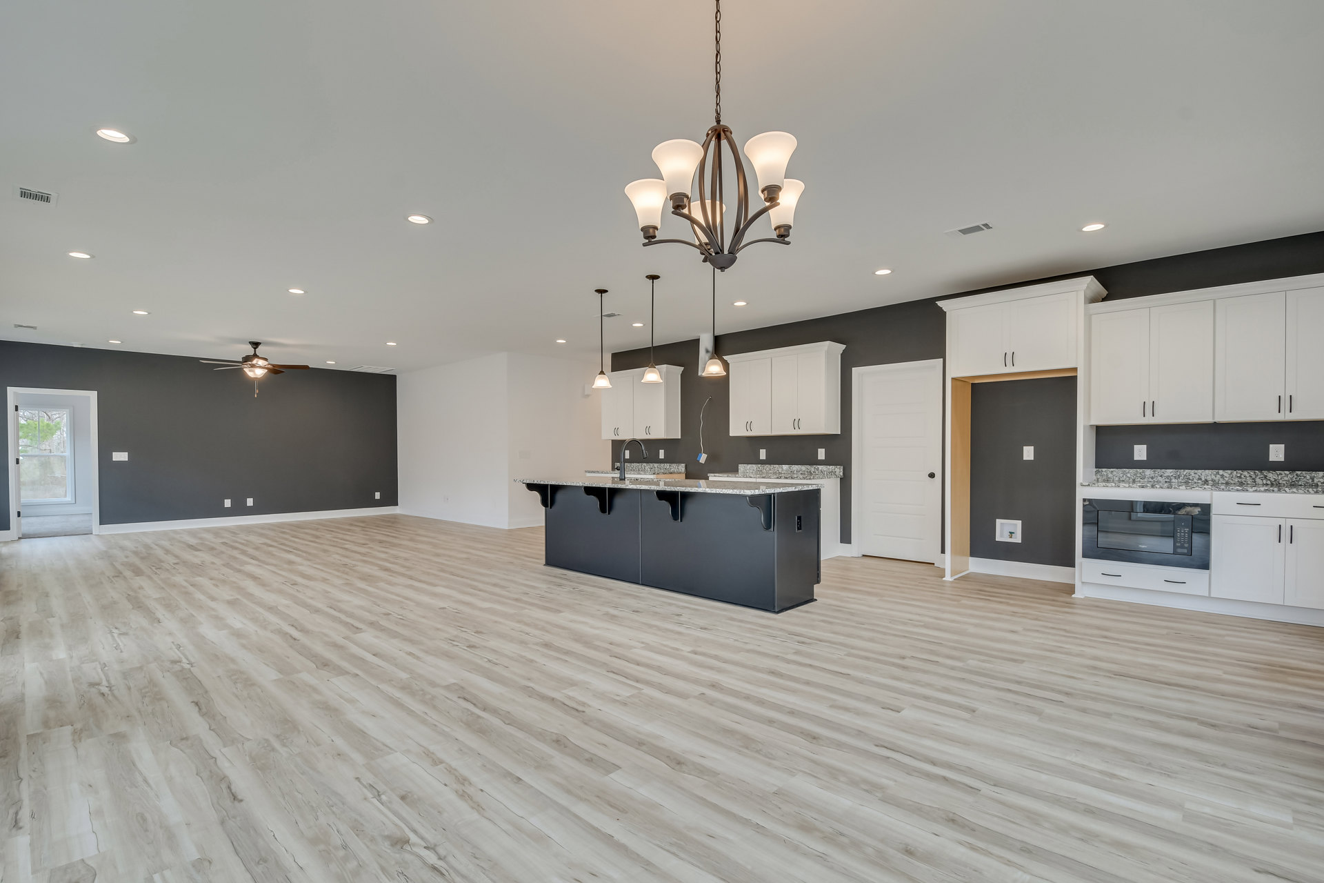 Spacious kitchen with marble island, modern cabinetry, chandelier, ceiling fan, large window overlooking trees, and light wood flooring