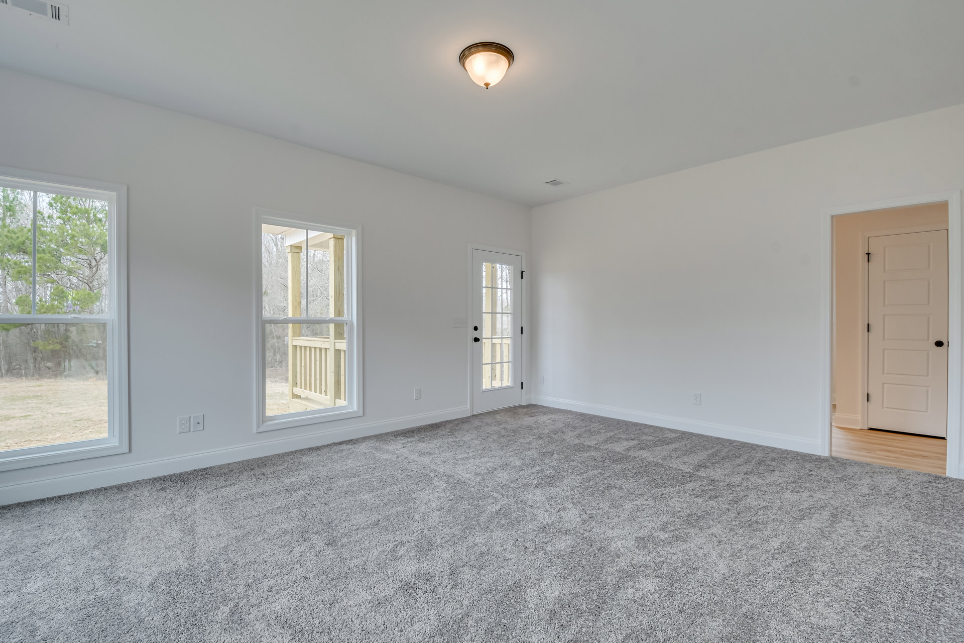 White paneled door with black handle, glass panes, beige carpet flooring, large windows with white trim, ceiling light fixture, smooth plaster walls