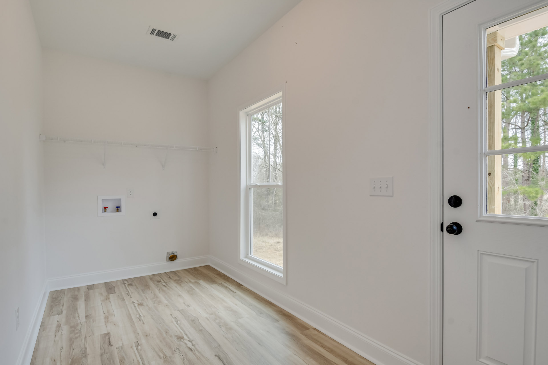 Wood floor room with large window overlooking trees, white wall with row of switches, built-in shelf featuring red and blue plumbing valves