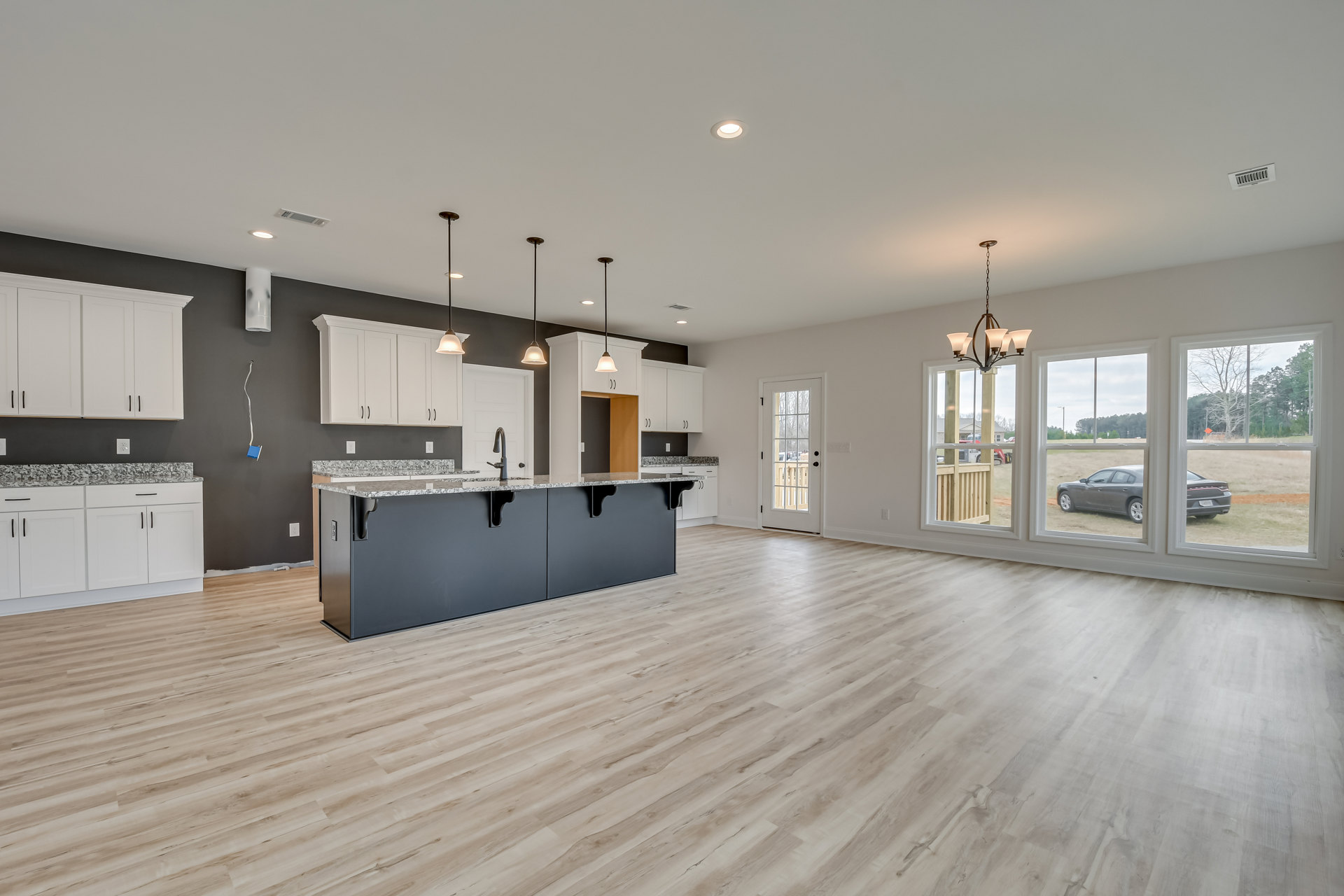 Open-concept kitchen and living room with hardwood flooring, black kitchen countertop with built-in sink, white cabinets featuring black trim, glass-paneled white door, car visible