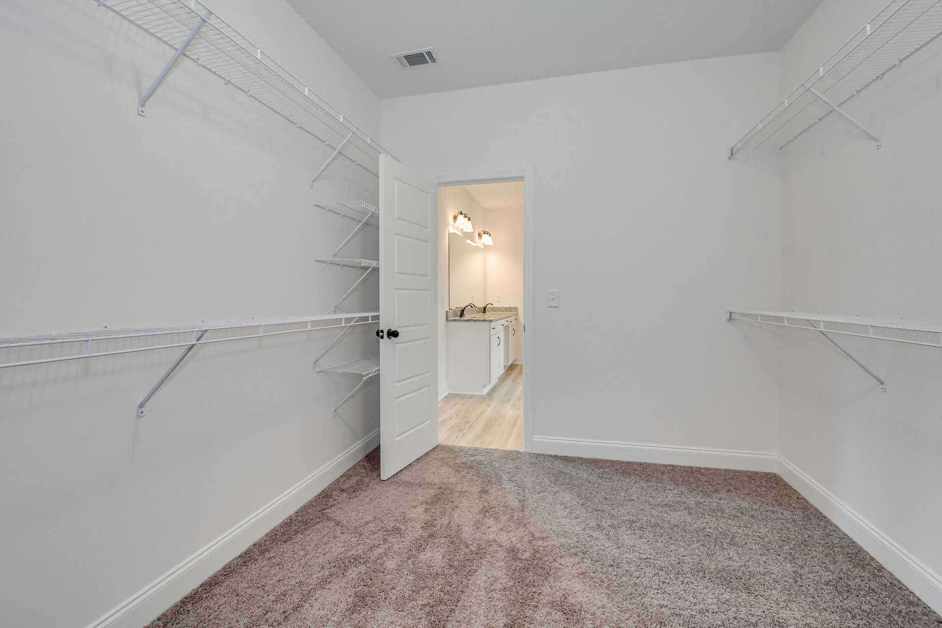Open doorway leading to a carpeted room with built-in white shelves, white kitchen counter with sink, and pendant lamp.