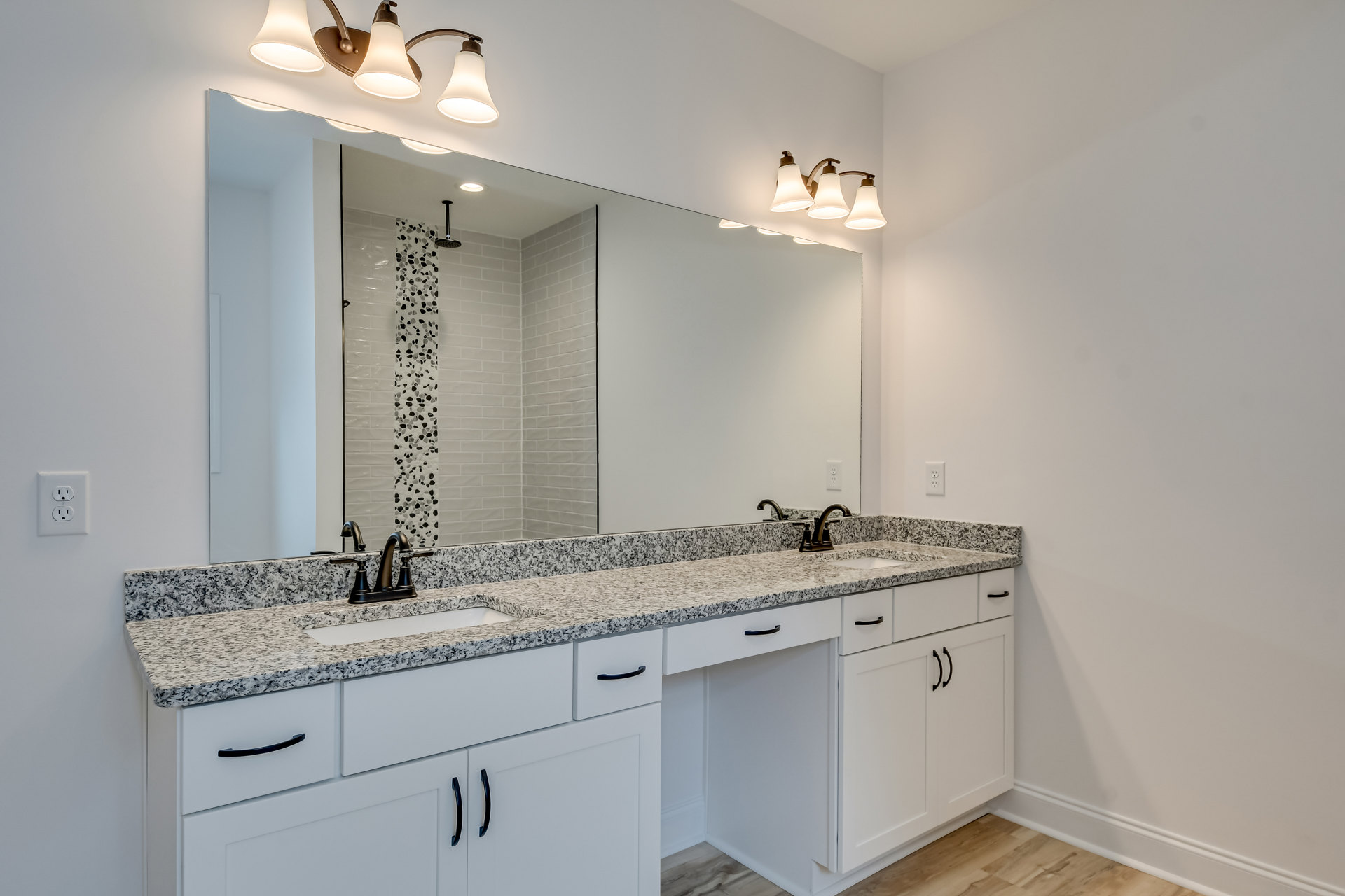 Bathroom with expansive mirror above marble countertops, modern light fixture with three lamps, tile backsplash, undermount sink, chrome faucet, and white cabinetry with drawers.