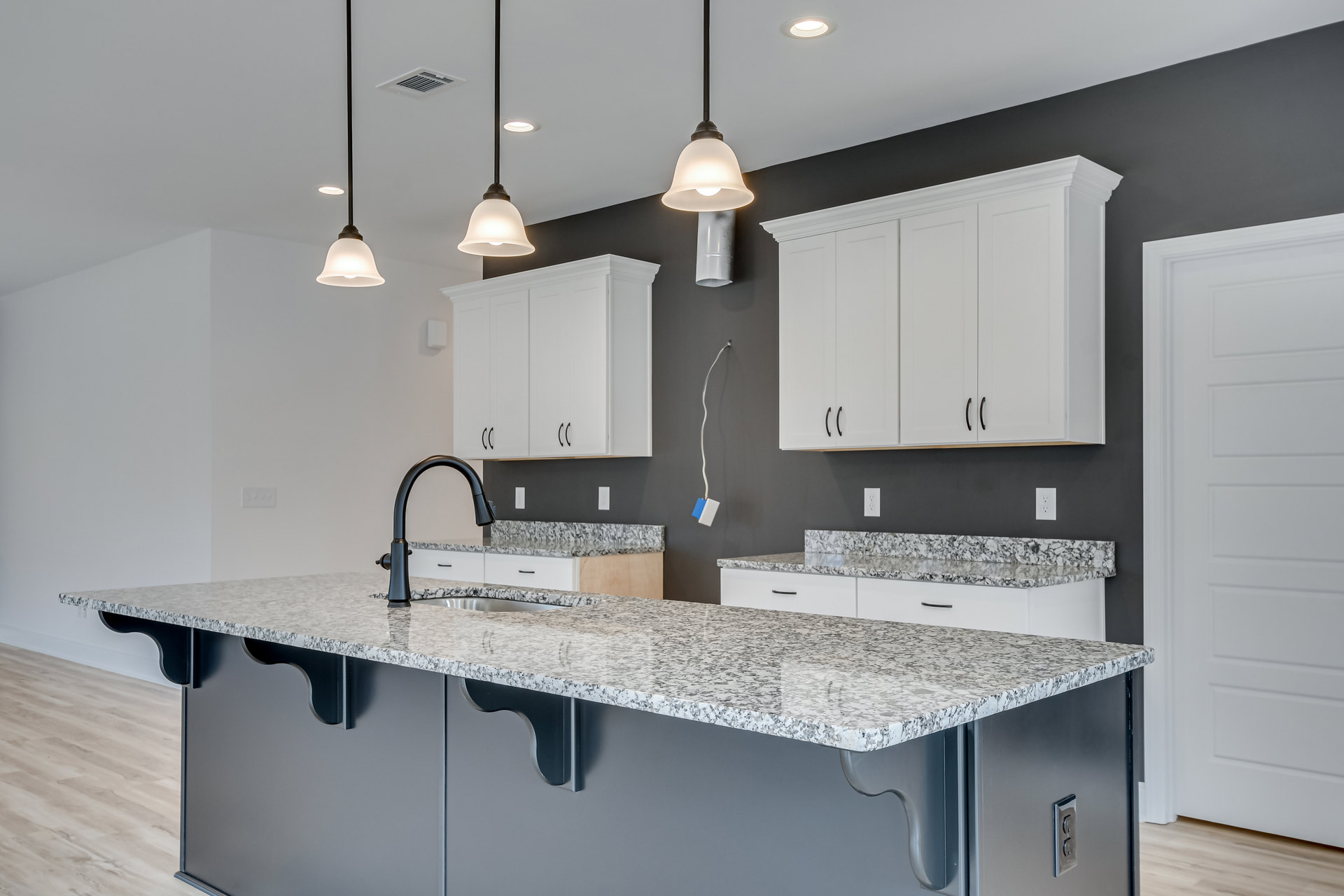 Granite countertops with undermount sink, white cabinets featuring black handles, stainless steel faucet, white door with black hardware, pendant light fixture above kitchen