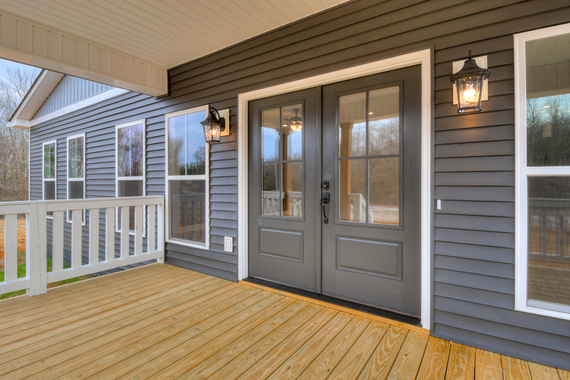Front porch with double wooden doors, white framed window, wood plank deck, white railing, and ceiling-mounted light fixture