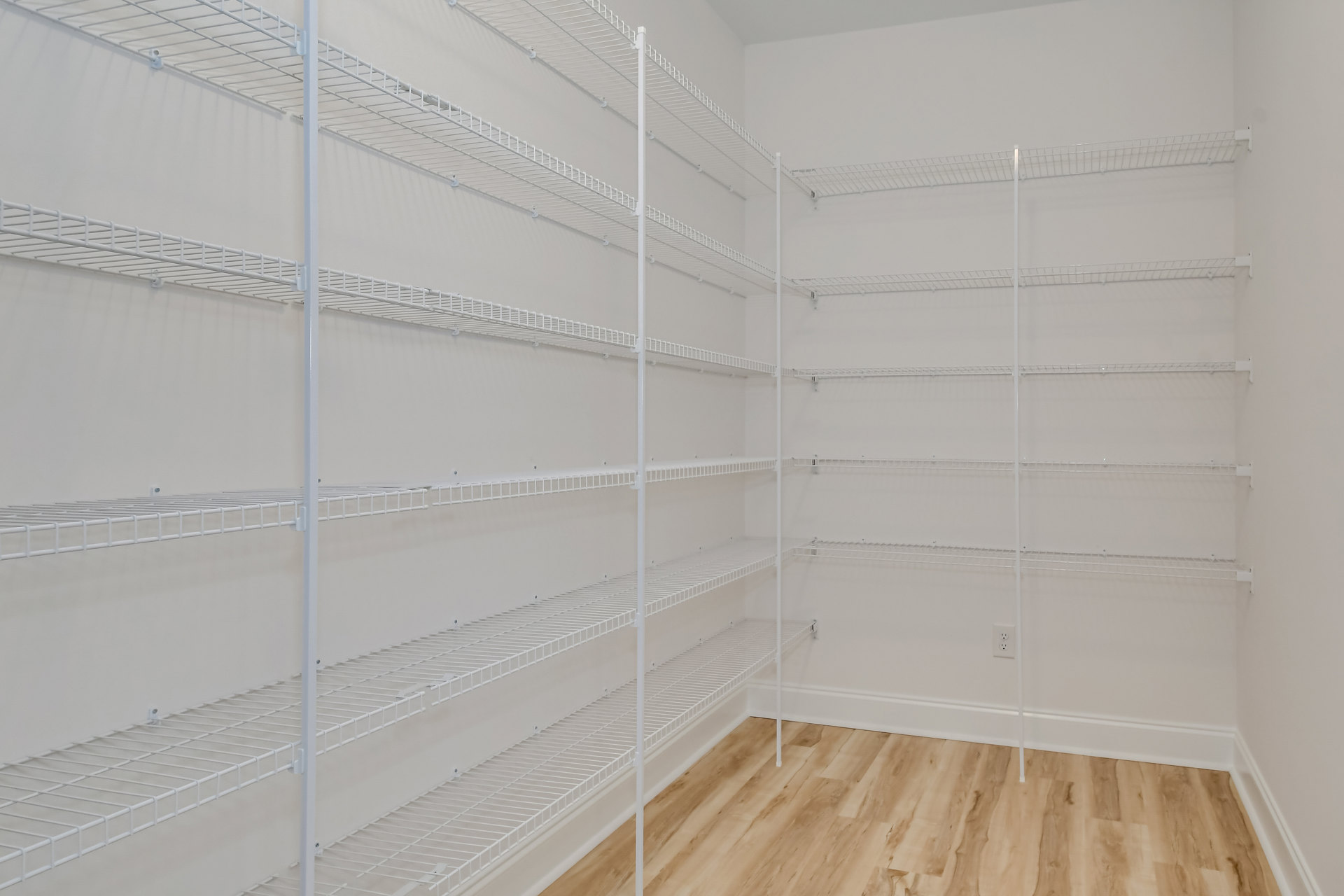 Empty closet with built-in white shelves against plaster walls and light flooring