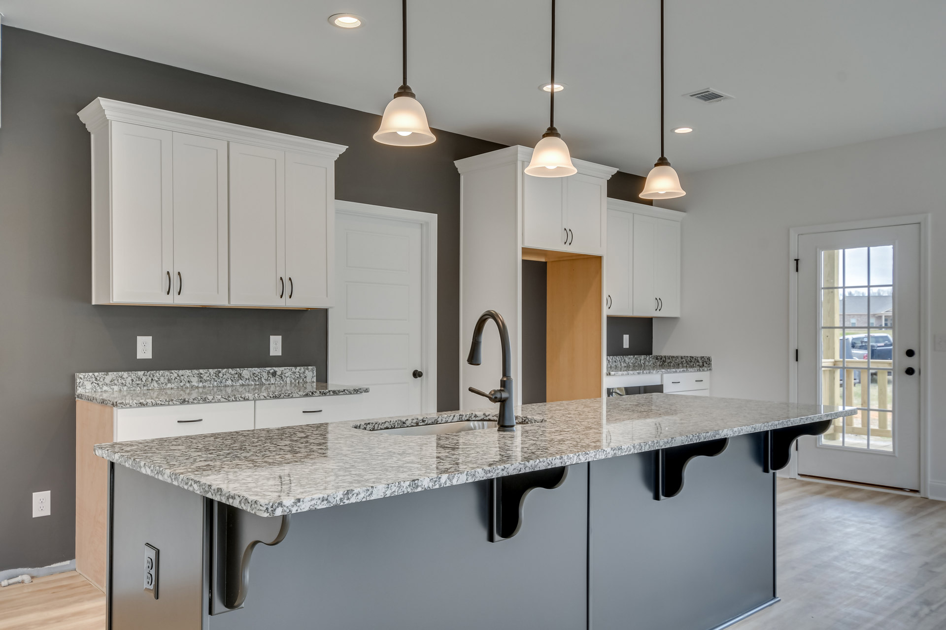 Granite countertop with undermount sink, white shaker cabinets, stainless steel faucet, tile backsplash, pendant light fixture, and kitchen appliances.