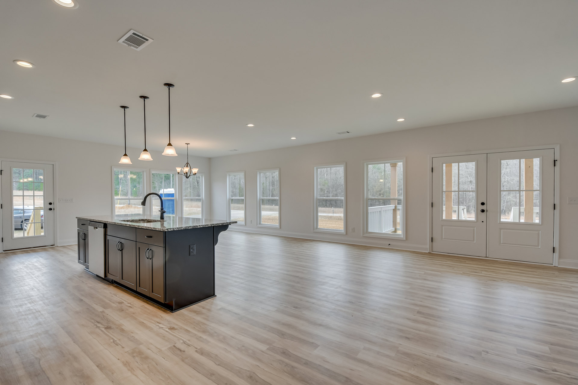 Spacious kitchen with wood flooring, central island featuring a sink, white cabinetry, large windows, double glass doors, and ceiling vent