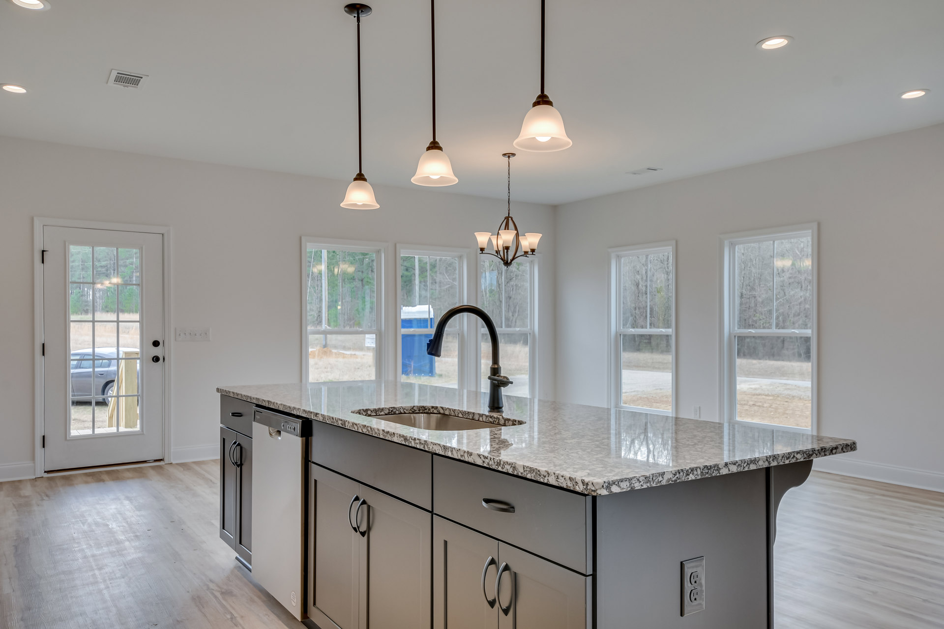 Spacious kitchen featuring a large central island with a built-in sink, white cabinetry, stone countertops, glass-paned door, and modern chandelier above