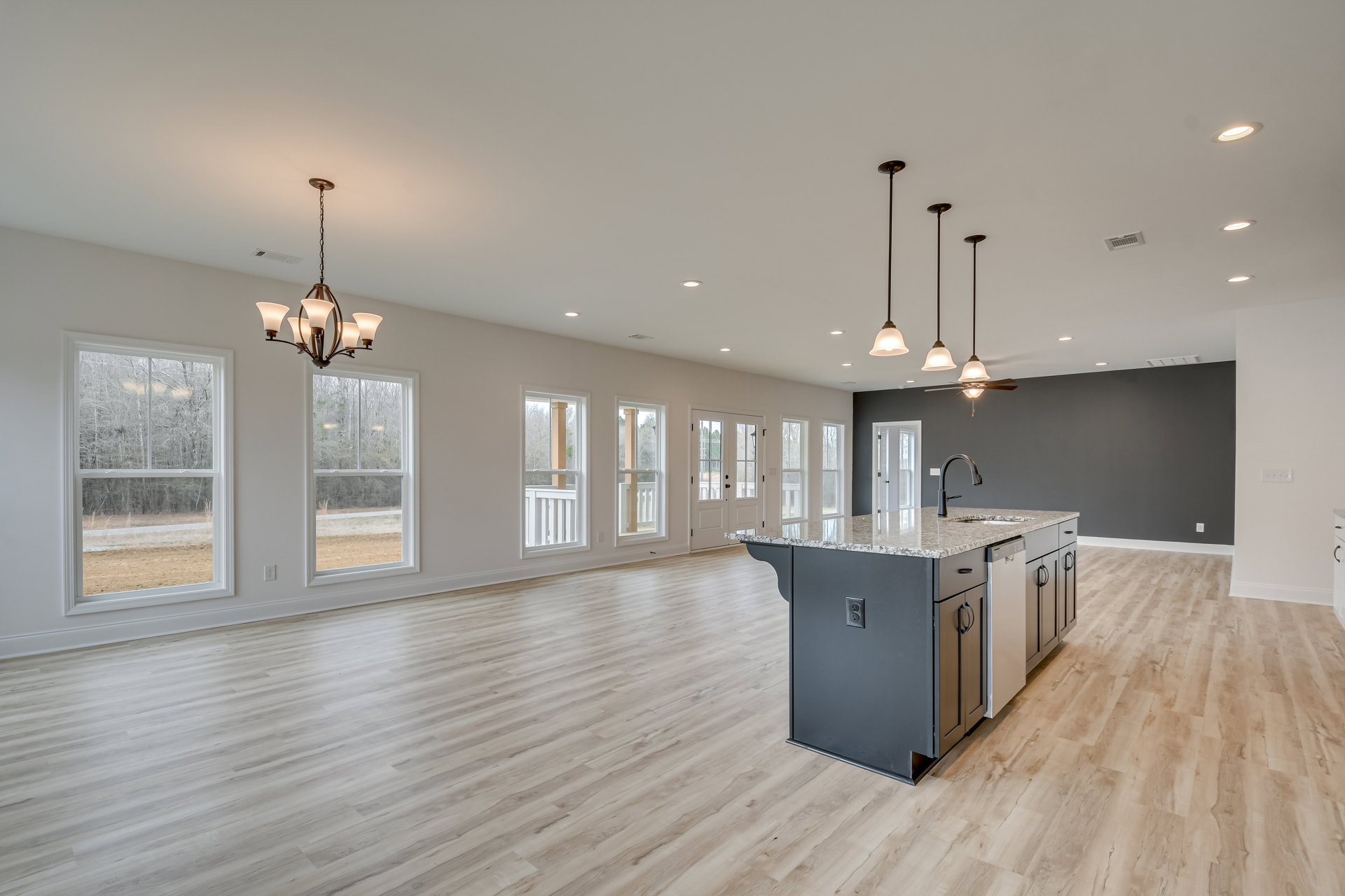 Open-concept kitchen and dining area featuring a wood floor, white cabinetry, granite kitchen island, large windows with tree views, and recessed ceiling lighting