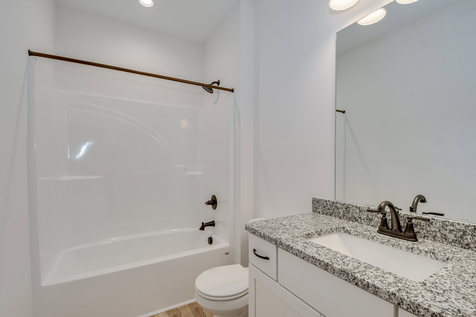 Modern bathroom featuring a white toilet with lid closed, rectangular sink and chrome faucet, white bathtub, and brown accent line on tiled wall.