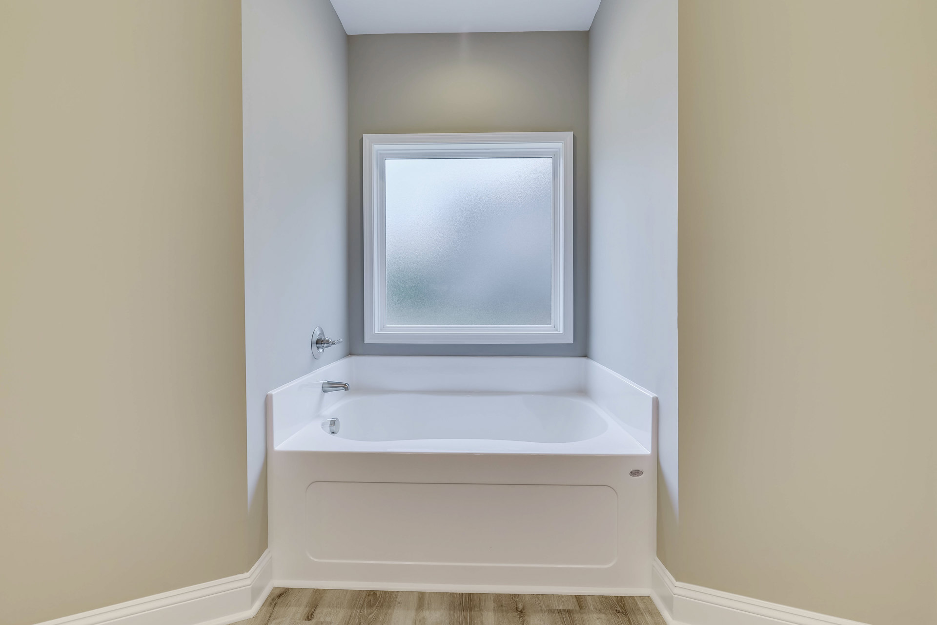 White freestanding bathtub with silver faucets beneath a square frosted glass window, surrounded by white plaster walls and ceiling in a modern bathroom.